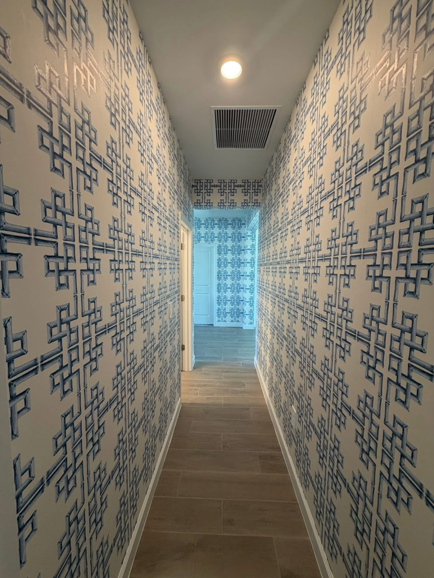Narrow corridor wrapped in cobalt fretwork wallpaper with wood floors